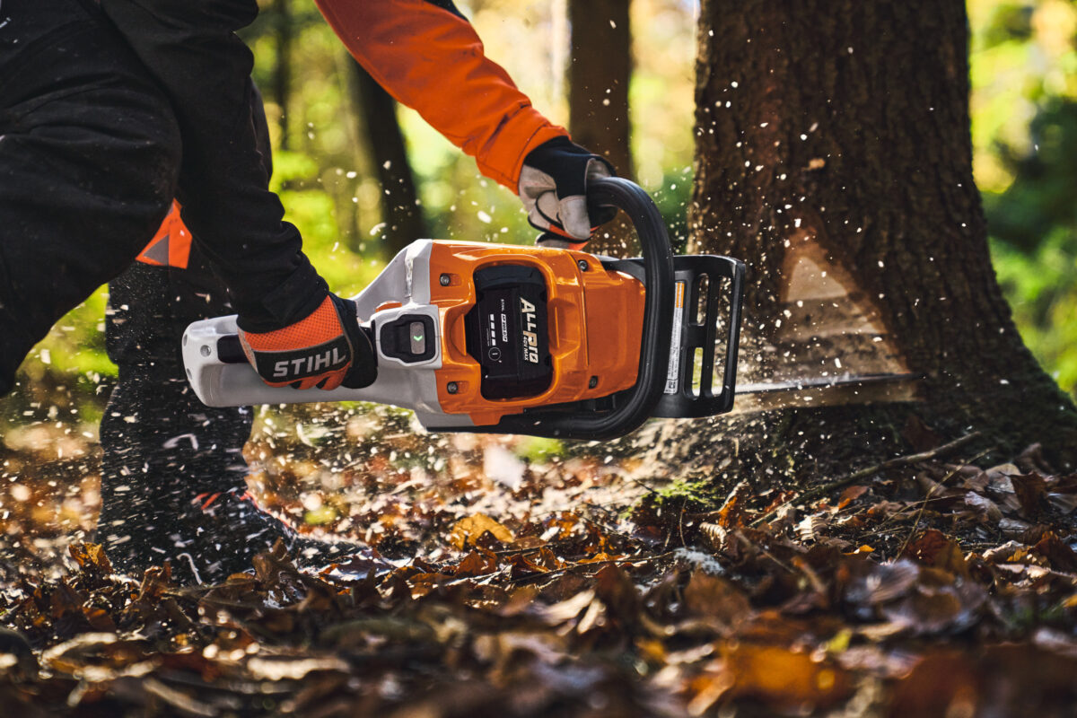 Person sägt mit einer STIHL ALLpro Akku-Kettensäge einen Baum im Wald, Sägespäne fliegen umher